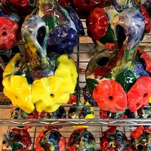 May include: A collection of colorful ceramic bottle stoppers with floral designs. The stoppers are arranged on a metal shelf with other decorative items.