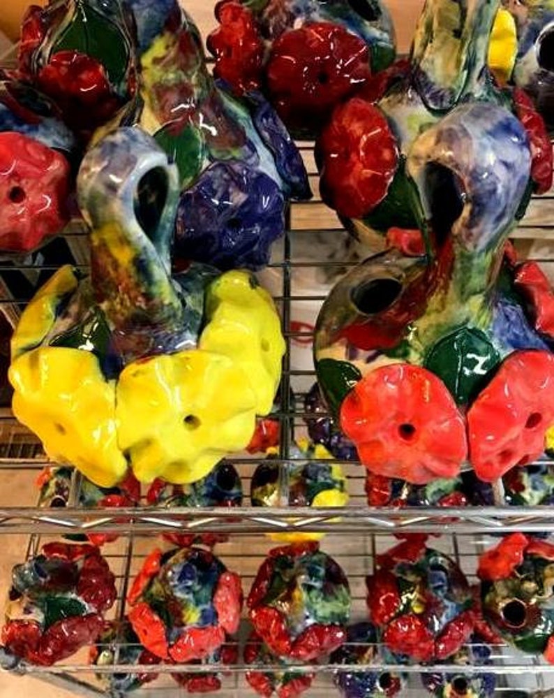May include: A collection of colorful ceramic bottle stoppers with floral designs. The stoppers are arranged on a metal shelf with other decorative items.