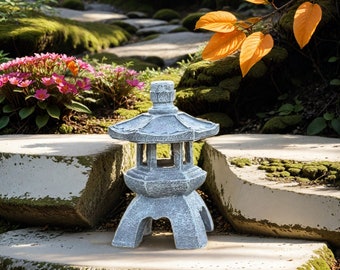 May include: A grey stone Japanese garden lantern with a multi-tiered design. The lantern has a pagoda-style roof and is set on a stone surface in a garden setting with a stone path, pink flowers, and orange leaves.