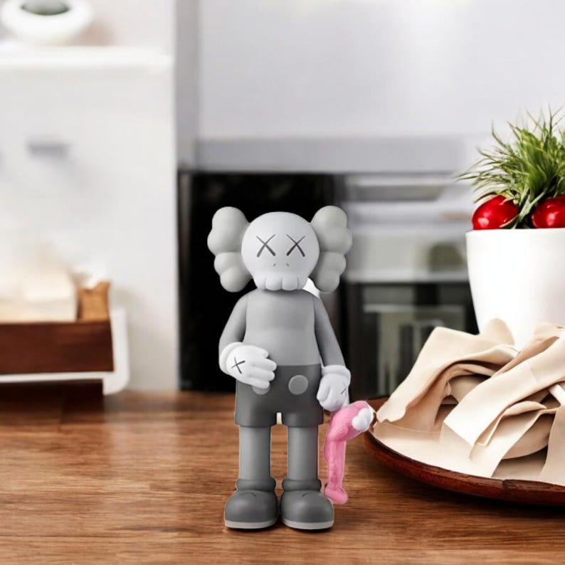 May include: A gray vinyl figure with a skull-like head and crossed-out eyes. The figure is wearing gray shorts, gloves, and shoes, and is holding a pink object. The figure is standing on a wooden surface.