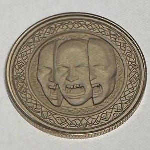 May include: Silver coin with a detailed design of three faces, each with a different expression, surrounded by an intricate pattern.