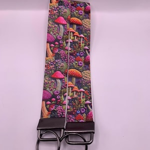 May include: A key fob strap with a detailed mushroom and floral pattern. The design features red, orange, and purple mushrooms set against a backdrop of flowers and foliage. The strap is attached to a metal key ring.