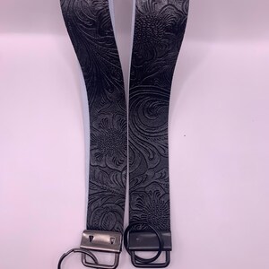 May include: Two black key fobs with a floral embossed pattern. Each fob has a metal clasp and a key ring. The key fobs are made of a durable material and are designed to hold keys securely.