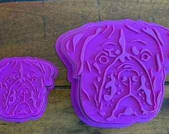 Może przedstawiać: Dwa fioletowe plastikowe wykrawacze do ciastek w kształcie psiej twarzy. Większy wykrawacz ma około 10 cm szerokości, a mniejszy około 5 cm. Twarz psa jest szczegółowa z oczami, nosem i zmarszczkami.