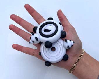 Może przedstawiać: Dwie 3D-drukowane zabawki w kształcie pand, w kolorze czarno-białym. Większa panda to pierścień z czarnym środkiem i białym zewnętrznym pierścieniem. Mniejsza panda to stos pierścieni z czarnym środkiem i białymi zewnętrznymi pierścieniami.