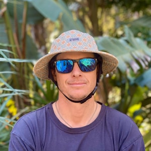 May include: A person wearing a blue and white patterned bucket hat with a black strap and blue mirrored sunglasses. The hat has the word "ZAKAA" printed on it.