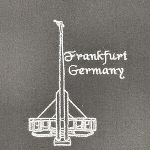 May include: White embroidered design of a building with the text "Frankfurt Germany" on a black fabric background.