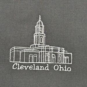 May include: Embroidered image of a building with a tall tower, rendered in white thread on a dark gray fabric. The text "Cleveland Ohio" is stitched below the building. The design is a simple, line-art style.