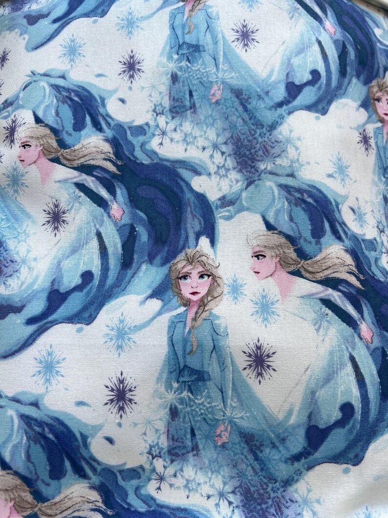 May include: A fabric featuring a repeating pattern of a character from the animated film, "Frozen." The design includes the character in a blue dress, surrounded by snowflakes and flowing blue and white elements.