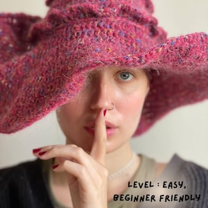 K&ouml;nnte beinhalten: Ein gro&szlig;er, strukturierter, magentafarbener H&auml;kelhut mit breiter Krempe und ger&uuml;schtem Oberteil. Der Hut hat blaue, gelbe und orangefarbene Flecken. Der Text "LEVEL: EASY, BEGINNER FRIENDLY" ist sichtbar.
