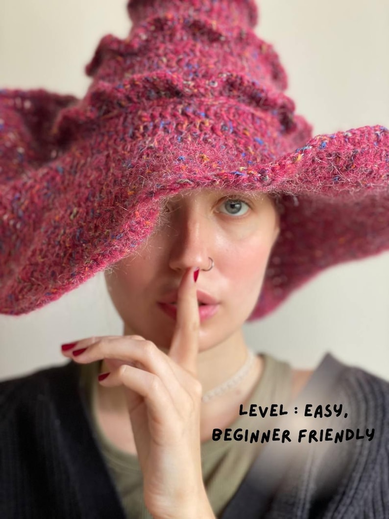 K&ouml;nnte beinhalten: Ein gro&szlig;er, strukturierter, magentafarbener H&auml;kelhut mit breiter Krempe und ger&uuml;schtem Oberteil. Der Hut hat blaue, gelbe und orangefarbene Flecken. Der Text "LEVEL: EASY, BEGINNER FRIENDLY" ist sichtbar.