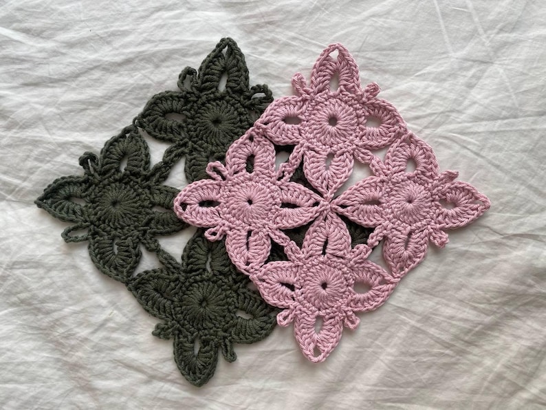 May include: Two crocheted square placemats, one in dark green and one in light pink, with a floral design.