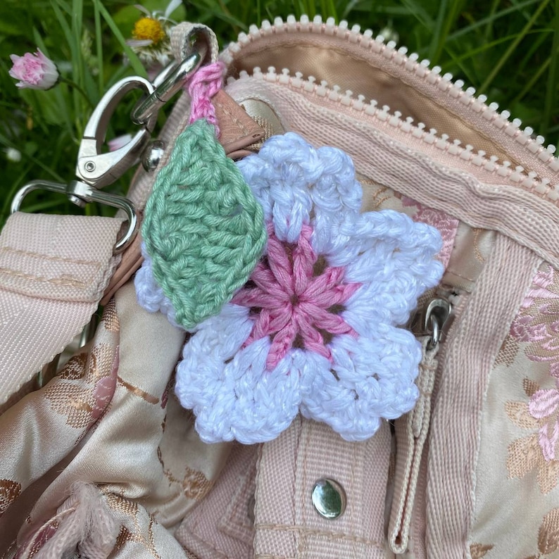 May include: A white crocheted flower with a pink center and a green crocheted leaf attached to a pink and brown fabric bag.