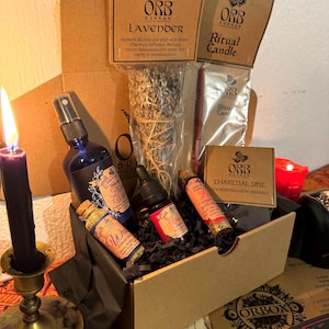 Può includere: Un set in scatola contenente vari oggetti spirituali. Include un flacone spray blu, piccole bottiglie, un mazzo di erbe, una candela e incenso. La scatola riporta la scritta "ORB DUKKAN LAVENDER" e "Ritual Candle".