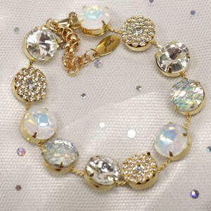 May include: A gold bracelet featuring a selection of round, clear and iridescent stones. The bracelet has a small tag with the word "Giski" on it.