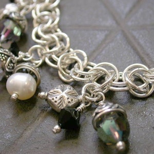 May include: A silver chain bracelet with multiple charms, including a pearl, a star-shaped charm, and several crystal beads. The charms are silver and black.