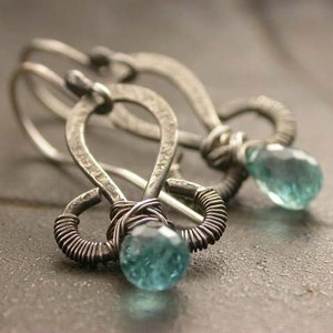 May include: A pair of silver earrings with blue teardrop-shaped gemstones. The earrings are made of wire and have a delicate, intricate design.