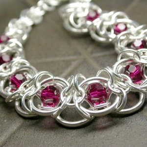 May include: A silver chain bracelet with a repeating pattern of interlocking rings and pink gemstones.