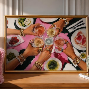 May include: A framed painting depicting a top-down view of multiple hands holding wine glasses in a toast over a bright pink tablecloth. The scene includes plates of food, including olives and sliced meat, with hands adorned in gold bracelets.