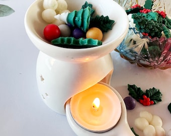 May include: White ceramic wax warmer with a tealight candle and a bowl filled with green, red, and white wax melts shaped like Christmas trees and holly leaves.