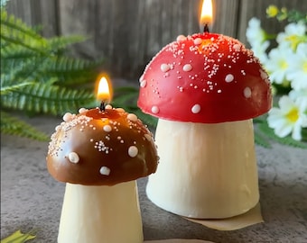 May include: Two mushroom-shaped candles, one red with white dots and one brown with white dots. Both candles have a white base.