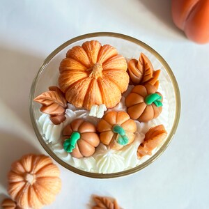 May include: A glass jar filled with white frosting and topped with orange and green pumpkin-shaped decorations. The frosting is decorated with leaves.