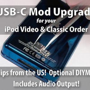 以下が含まれることがあります： USB-Cポートに改造中のダークブルーのiPod VideoおよびClassicデバイス。金属製のピンセットが、小さなUSB-Cコンポーネントを背面ケースの上で保持しています。画像内のテキストは「USB-C Mod Upgrade for your iPod Video & Classic Order」と書かれています。