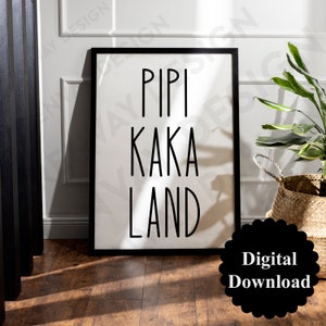 Puede incluir: Arte de pared imprimible en blanco y negro con el texto "Pipi Kaka Land" en una fuente simple y moderna. El arte está enmarcado en un marco negro y se muestra en un suelo de madera clara.