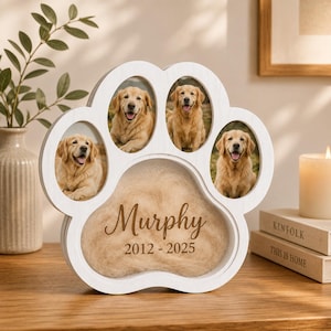 May include: A white paw-shaped wooden memorial frame featuring four oval photo slots containing pictures of a golden retriever. The central pad area displays the name Murphy and the years 2012-2025 engraved in a brown script and sans-serif font.