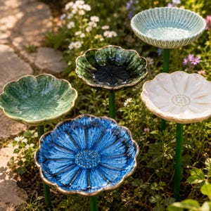 May include: Five flower-shaped garden stakes with glazed ceramic bowls in blue, light blue, dark green, light green, and white. Each bowl features a scalloped edge and a central textured pattern, mounted on a thin green metal rod for garden display.
