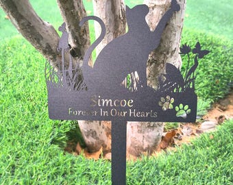 May include: A black metal garden stake featuring a cat silhouette reaching for a butterfly. The stake includes the name "Simcoe" and the phrase "Forever In Our Hearts". Decorative paw prints and floral elements are also present.