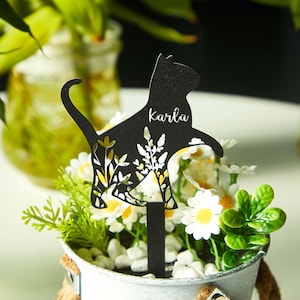 May include: A black cat-shaped garden stake with the name "Karlu" cut out. The stake features a floral design and is placed in a small white bucket filled with flowers and greenery. The bucket has a rope handle.