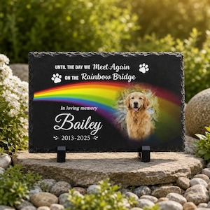 May include: A rectangular black slate memorial plaque featuring a colorful rainbow graphic, a photographic portrait of a golden retriever, and the text: UNTIL THE DAY WE Meet Again ON THE Rainbow Bridge, In loving memory Bailey, 2013-2025.