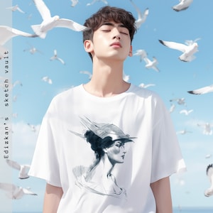 Op de afbeelding: Een wit T-shirt met een zwart-witte schets van een vrouw met een hoed op de voorkant. De achtergrond is een blauwe lucht met witte vogels die vliegen.