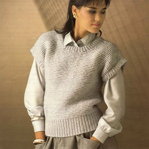 May include: A woman wearing a white shirt and a light gray sleeveless sweater vest. The sweater vest is knit with a chunky yarn. The text on the label reads "Patons Diana Brushed Chunky 76-102 cm 30-40 in Price Code B 7316".