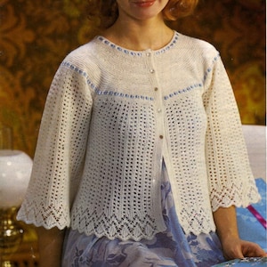 May include: A white crocheted cardigan with blue trim and a button closure. The cardigan has a lacy pattern and is shown on a model wearing a floral dress. The pattern number is 3202 and the yarn is 4 ply. The pattern is for four sizes, 34 to 40 inches.