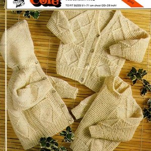 Op de afbeelding: Een set van drie gebreide truien in een crèmekleur. De truien hebben een ruitpatroon en zijn ontworpen voor kinderen. De truien zijn gelabeld met "King Cole Bosun Aran Knitting" en "KC 441".