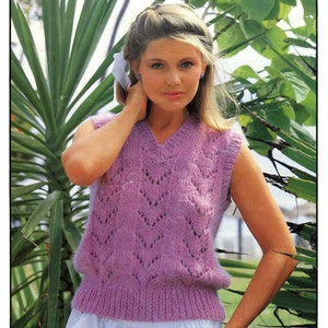 May include: A purple sleeveless knitted vest with a lacy pattern. The vest is made with chunky yarn and has a V-neck. The pattern number is 1858.