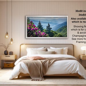 The image is a modern bedroom with a large bed, wooden furniture, and a framed landscape photograph hanging on the wall.