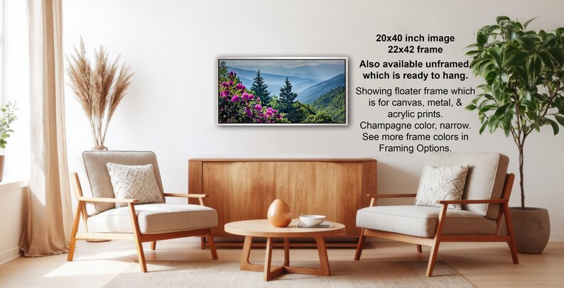 a living room with a wooden coffee table, two white armchairs, and a potted plant. A framed landscape photograph is hanging on the wall, and there is text providing information about the frame options.