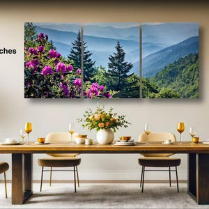 a large, three-panel landscape painting hanging on a wall above a wooden dining table with four chairs. The painting depicts a scenic mountain landscape with purple flowers in the foreground.