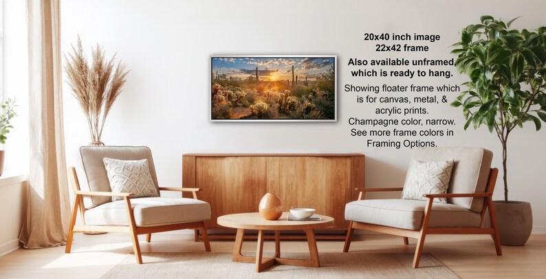 a living room with a wooden coffee table, two white armchairs, and a potted plant. Above the coffee table, there is a framed landscape painting hanging on the wall.