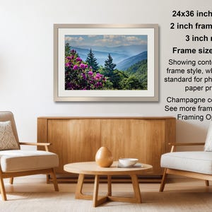 a living room with a wooden coffee table, two white armchairs, and a framed landscape photograph hanging on the wall.