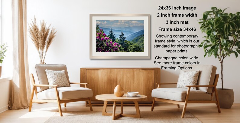 a living room with a wooden coffee table, two white armchairs, and a framed landscape photograph hanging on the wall.