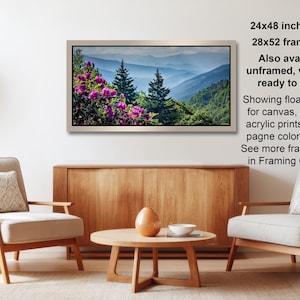 a living room with a wooden coffee table, two white armchairs, and a framed landscape photograph hanging on the wall.