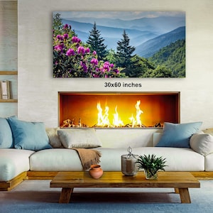 a cozy living room with a fireplace, a large framed landscape painting depicting a mountainous scene with pink flowers, and a wooden coffee table in front of the fireplace.