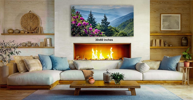 a cozy living room with a fireplace, a large framed landscape painting depicting a mountainous scene with pink flowers, and a wooden coffee table in front of the fireplace.
