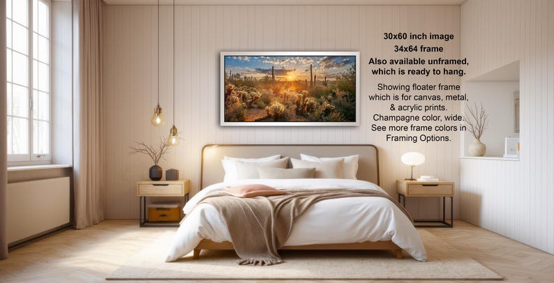 The image is a modern bedroom with a large bed, wooden furniture, and a framed landscape painting hanging on the wall. The painting depicts a desert scene with a sunset. The room has a minimalist and clean design, with a white color scheme and natural elements like a vase and a plant.