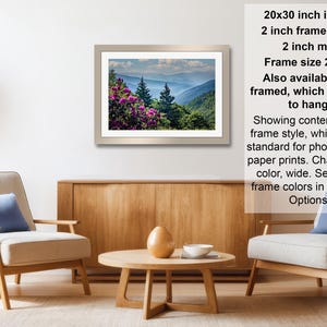 a living room with a framed landscape photograph hanging on the wall, a wooden coffee table in the center, and two armchairs facing each other.