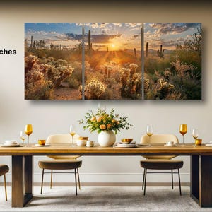 a large, framed desert landscape painting hanging on a wall above a wooden dining table set with wine glasses, plates, and a vase of flowers.